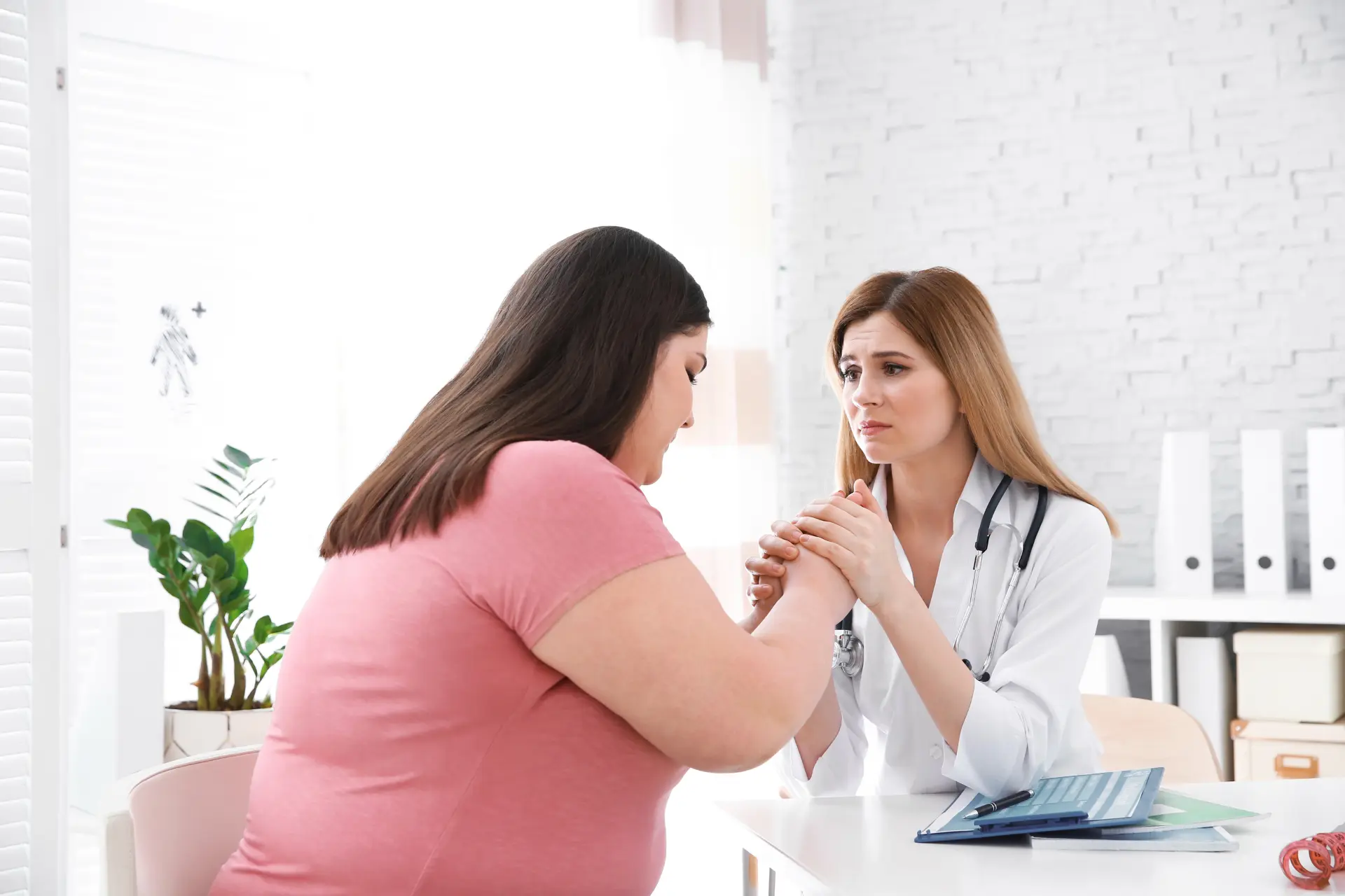 Doctora empática consultando a una paciente con sobrepeso en una clínica luminosa.