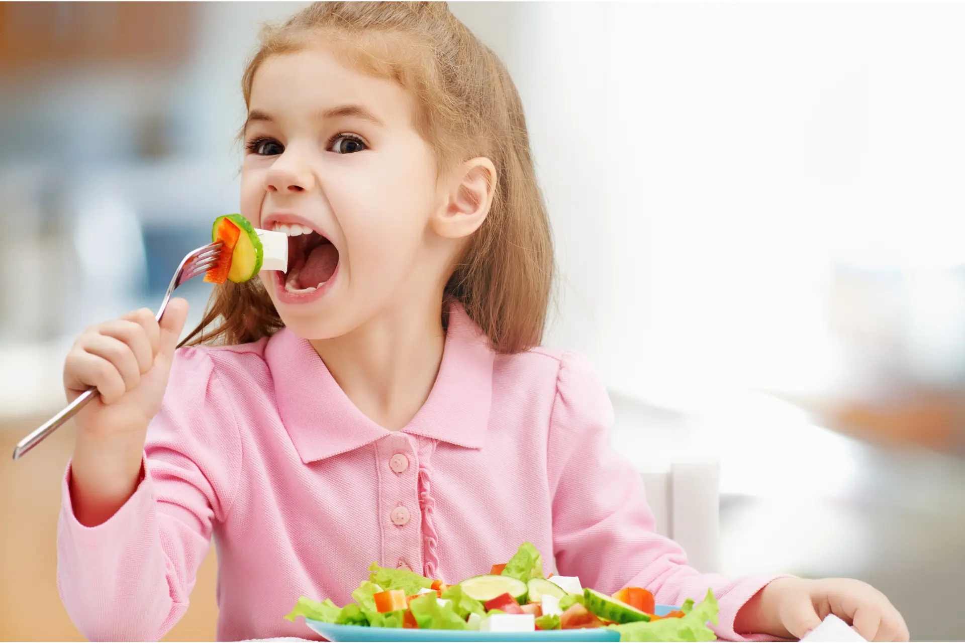 Niña comiendo una ensalada saludable en la mesa.