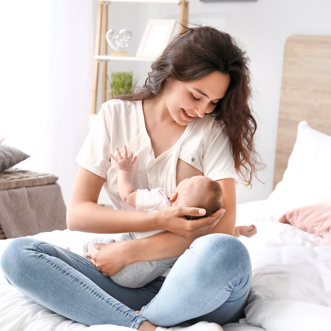Mujer sonriente amamantando a su bebé, representando el postparto y bienestar.