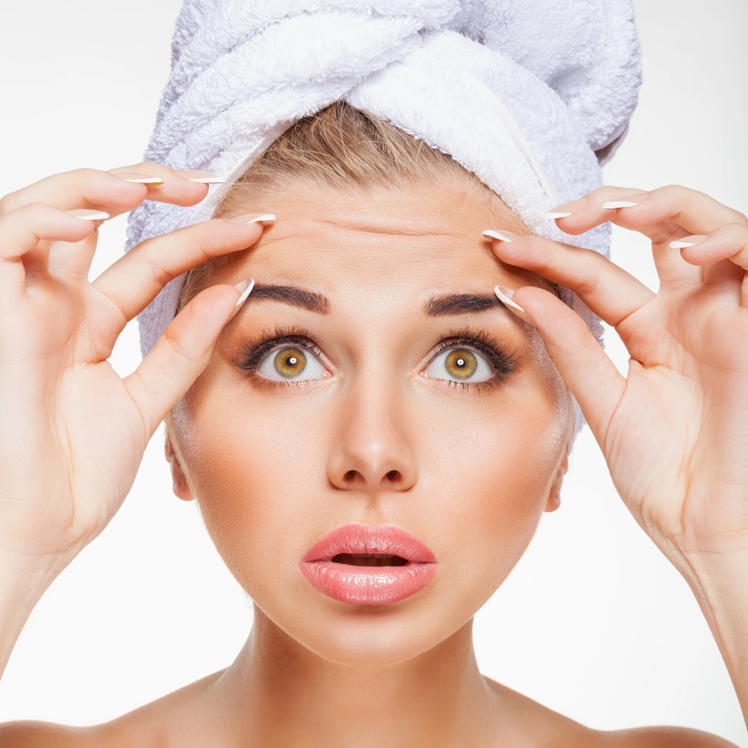 Mujer preocupada por sus arrugas en la frente, buscando una solución estética.
